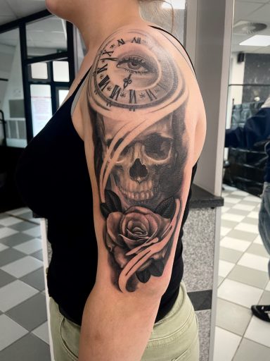 Tattoo auf dem Oberarm: Totenkopf, Uhr und Rose in Schwarz-Weiß.