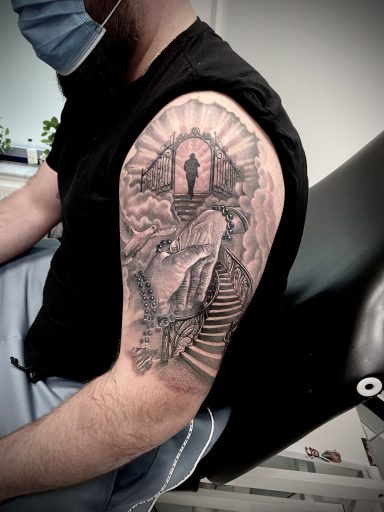 Männlicher Arm mit detailliertem Tattoo einer Treppe und einer stilisierten Figur.