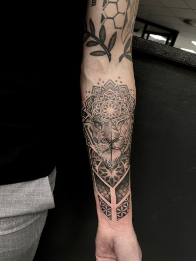 Tattoo auf dem Unterarm mit einem geometrischen Muster und einem Löwenkopf.