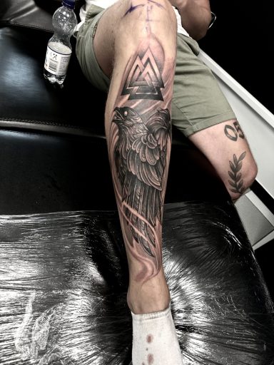 Tattoo eines Vogelmotivs auf dem Schienbein, umgeben von geometrischen Formen.