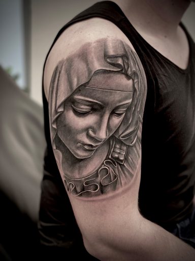 Schwarz-weißer Tattoos eines nachdenklichen Gesichts unter einem Kopftuch auf einem Arm.