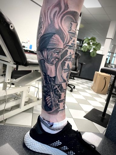 Schwarzes Tattoo auf dem Oberschenkel mit detaillierten Illustrationen und Schattierungen.