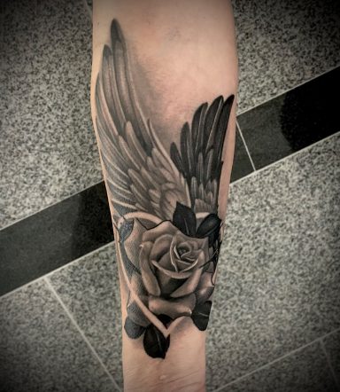 Schwarz-weiße Tätowierung eines Flügels über einer Rose auf dem Unterarm.