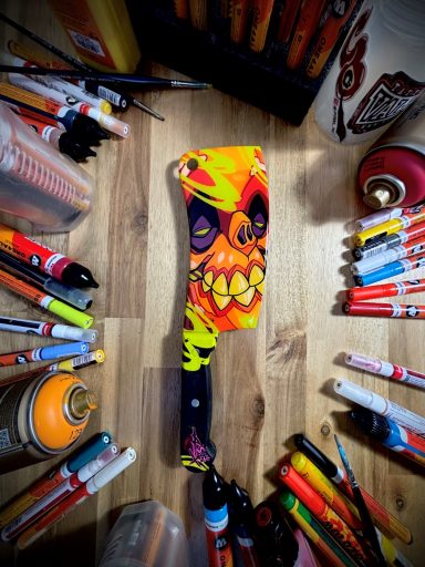 Bunte Spraydose mit auffälligem Gesichtsdesign, umgeben von verschiedenen Markern.