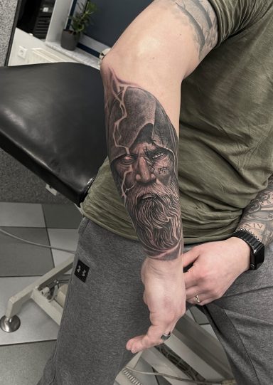 Tattoo eines älteren Mannes mit Bart und eindrucksvoller Mimik auf dem Unterarm.
