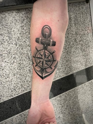 Schwarz-weißer Anker-Tattoo mit einem Steuerrad auf dem Unterarm.