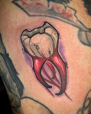 Tattoo eines glänzenden Zahns mit roten Wurzeln auf der Haut.