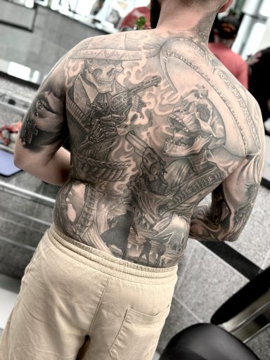 Mann mit detaillierten Tattoos auf dem Rücken, steht in einem hellen Raum.
