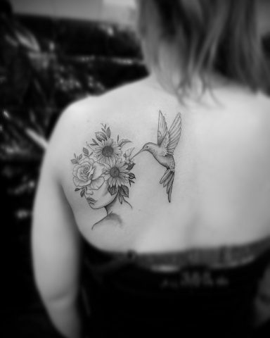 Tattoo auf dem Rücken einer Person, zeigt eine Blume und einen Kolibri.