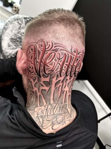 Tattoo mit künstlerischen Schriftzügen auf dem Hinterkopf eines Mannes.