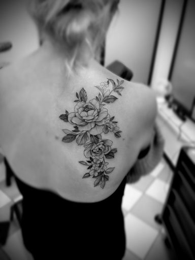 Schwarze Tätowierung von Blumen und Blättern auf dem Rücken einer Person.
